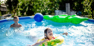 Swimming Pool im Garten mit spielenden Kindern. Die Kids planschen im Wasser und haben Spaß. Das Planschbecken ist gefüllt mit kaltem Wasser.