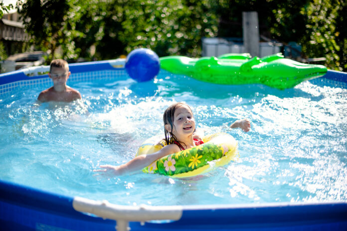 Swimming Pool im Garten mit spielenden Kindern. Die Kids planschen im Wasser und haben Spaß. Das Planschbecken ist gefüllt mit kaltem Wasser.