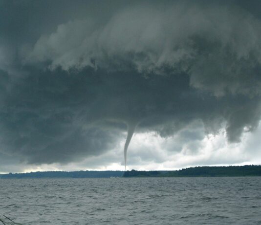 Über einem großen See kann man einen Tornado erkennen. Es herrscht Unwetter und das Wasser ist sehr unruhig. Der Himmel ist mit dunklen Wolken verhangen.