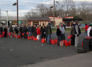 Warteschlange mit Kanistern an Tankstelle.