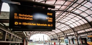 Wartezeiten-Schild an der Haltestelle. Der Bahnhof hat mehrere Gleise, die relativ leer sind. An diesem Hauptbahnhof steht auch kein Zug. Es werden nur die Abfahrtszeiten angezeigt.