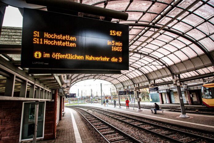 Wartezeiten-Schild an der Haltestelle. Der Bahnhof hat mehrere Gleise, die relativ leer sind. An diesem Hauptbahnhof steht auch kein Zug. Es werden nur die Abfahrtszeiten angezeigt.