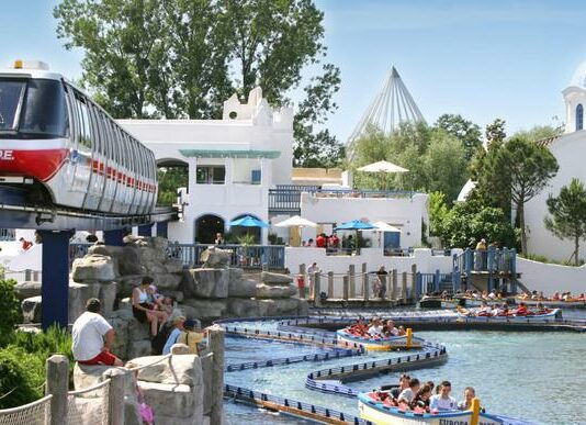 Attraktionen im Europapark. Links fährt eine schwebende Hochseilbahn über den Köpfen der Besucher hinweg. Rechts befindet sich Wasserpark. Der Freizeitpark lockt mit zahlreichen Events.