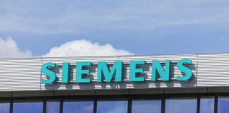 Das Siemens Geschäftsgebäude mit großem türkisem Schriftzug des Logos und des Namens. Darüber sieht man den strahlend blauer Himmel mit einigen Wolken.