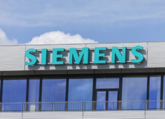 Das Siemens Geschäftsgebäude mit großem türkisem Schriftzug des Logos und des Namens. Darüber sieht man den strahlend blauer Himmel mit einigen Wolken.