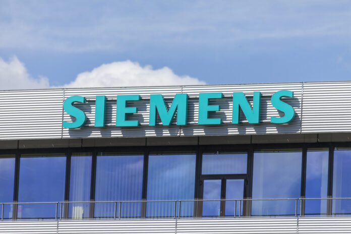 Das Siemens Geschäftsgebäude mit großem türkisem Schriftzug des Logos und des Namens. Darüber sieht man den strahlend blauer Himmel mit einigen Wolken.