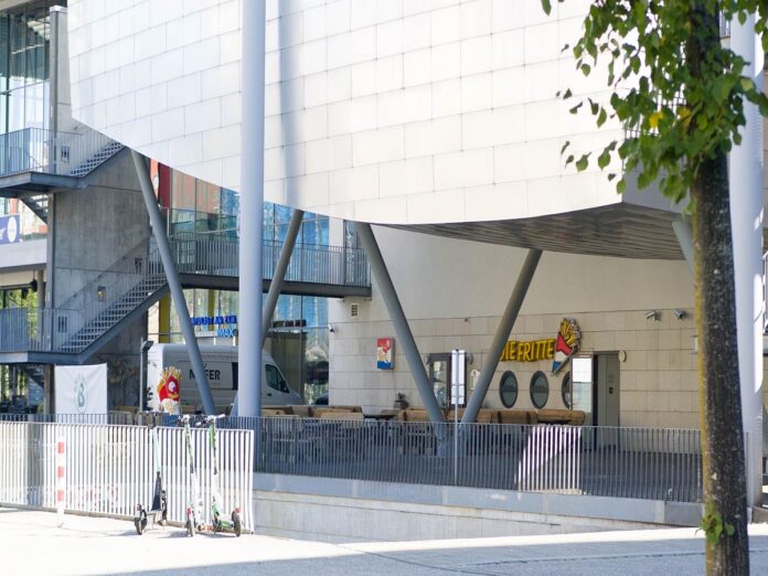 Restaurant am Filmpalast in Karlsruhe. Von außen sind nur der Eingang, die Fassade, Gehweg, Mauer, Straße und das Gebäude zu sehen.