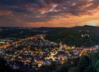 Über einer Stadt geht gerade die Sonne am Horizont unter. Die Lichter leuchten in der Stadt, die aus der Luft zu sehen ist.