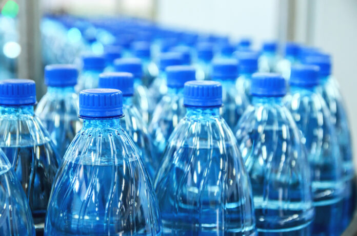Hunderte von blauen Getränkeflaschen in der Produktion. Sie stehen eng nebeneinander auf einem Laufband. Die Plastikflaschen haben noch keine Etiketten und sind blau.