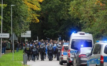 Abgesperrte Straße mit Blaulicht. Die Polizisten sind in einer großen Besatzung unterwegs ebenso mit mehreren Einsatzfahrzeugen auf den Straßen. Das ist ein Großeinsatz.