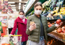 Zwei Frauen gehen in einem Supermarkt oder einem Discounter mit einer Maske einkaufen. Offensichtlich befinden sich die Menschen hier gerade in einer Pandemie.