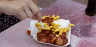 Eine Person ist Currywurst mit Pommes