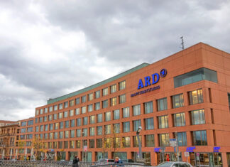 Das Gebäude des ARD-Hauptstadtstudios mit dem Logo der ARD in Blau am oberen Teil des Gebäudes. Das Gebäude aus Backstein ist riesig und beherbergt viele Räume. Vor dem Gebäude laufen einige Menschen.