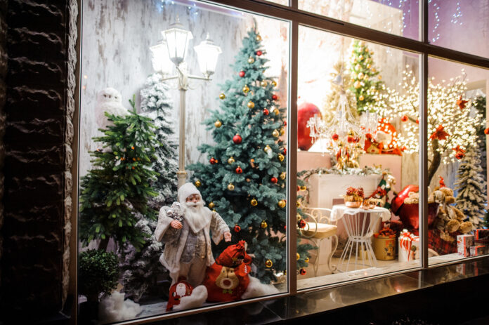 Es ist Weihnachten. Ein liebevoll dekoriertes Schaufenster in einem Kaufhaus zeigt eine Weihnachtsszene. Man sieht einen Weihnachtsmann und mehrere Weihnachtsbäume mit Weihnachtskugeln. Ein helles, warmes Licht zeigt einen mit Geschenken dekorierten Tisch.