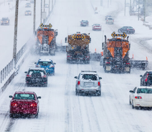 Der Blick auf eine mehrspurige Autobahn im tiefsten Winter und es scheint sehr kalt zu sein. Ein Schneesturm fegt über die befahrenen Straßen. Autos und Lkws haben ihre Lichter an und bahnen sich ihren Weg durch die eingeschneiten Straßen.