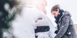 Eine Frau in Winterjacke befreit ihr Auto von Schnee und Eis.