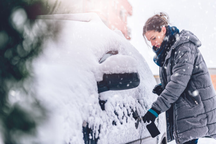 Eine Frau in Winterjacke befreit ihr Auto von Schnee und Eis.