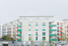 Ein neues Wohnviertel in der Stadt bestehend aus Häuserblöcken mit Flachdach, vielen Stockwerken und seitlich herausragenden Balkonen, vor denen einige Autos parken.