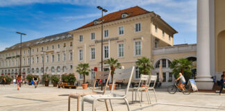 Der Marktplatz in Karlsruhe bei Sonnenschein, in der Mitte stehen Stühle. Ein Stuhl steht in der Sonne in der Innenstadt, ohne einen Bürger oder einen Gast.