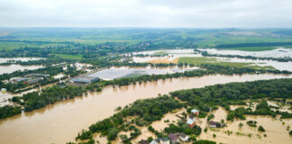 Überschwemmtes Hochwasser-Gebiet von oben. Die Häuser und Straßen sind überflutet vom Wasser. Der kritische Pegelstand ist überschritten. Die Bürger bringen sich in Sicherheit.