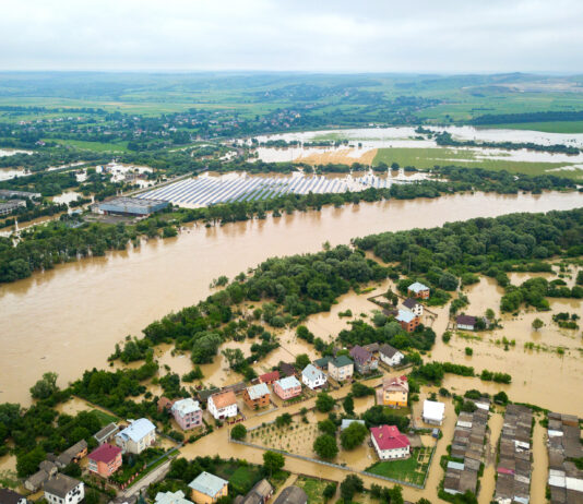 Überschwemmtes Hochwasser-Gebiet von oben. Die Häuser und Straßen sind überflutet vom Wasser. Der kritische Pegelstand ist überschritten. Die Bürger bringen sich in Sicherheit.