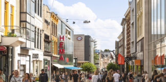 Passanten schlendern durch eine Einkaufsstraße in einer Großstadt bei schönem Wetter