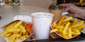 Ein Tablet mit Pommes und Getränk bei McDonalds. In der Mitte steht ein Becher gefüllt mit einem Milchshake oder mit einem Softdrink, wie Cola, Fanta oder Sprit. Im Hintergrund steht ein Becher Kaffee auf dem Tisch in der Mc Donalds Filiale.