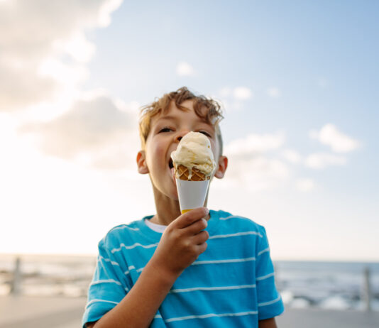 Eine Junge am Strand isst ein Eis.