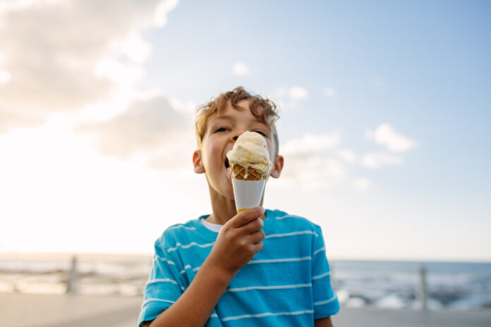 Eine Junge am Strand isst ein Eis.