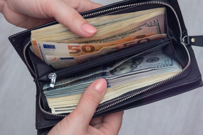 Frauenhände öffnen Portmonnaie, welches Euro und Dollarscheine offenbart