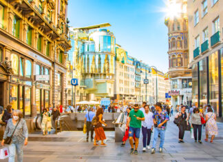 Passanten laufen durch eine Altstadt an Laden Filialen vorbei und gehen einkaufen