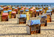 Typischer Strandkorb mit Sonnensegel an der Ostsee. Die Strandkörbe sind mit roten und blauen Abdeckungen als Sonnenschutz versehen. Urlauber können diese Strandkörbe mieten und tagsüber im Sand vor Sonne und Wind schützen.