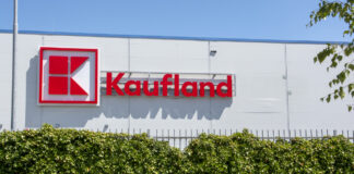 Ein große Kaufland-Filiale in einem großen Gebäude. Davor befindet sich eine hochgewachsene Hecke. Auf dem weißen Gebäude befindet sich das rot-weiße Kaufland-Logo sowie der rote Schriftzug Kaufland.