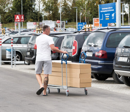 Ein Kunde schiebt seinen Einkauf – verpackt in großen Kartons – über einen Parkplatz von Ikea. Er benutzt für den Transport einen großen Einkaufswagen speziell für Pakete.