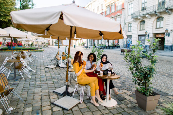 Drei jungen Frauen sitzen auf einer Terrasse unter einem Sonnenschirm