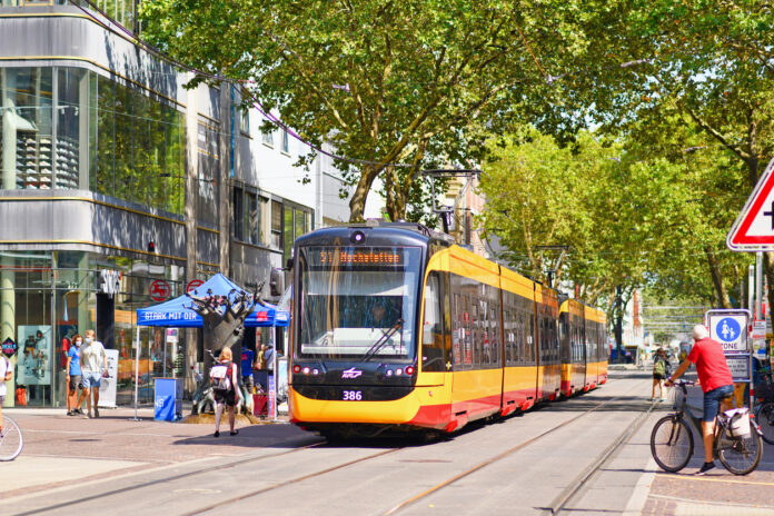 Eine Straßenbahn fährt durch eine Karlsruher Einkaufsstraße. An der Haltestelle steigen Fahrgäste ein und aus. Sie lösen ein Ticket für die Bahn, um im ÖPNV zu fahren.