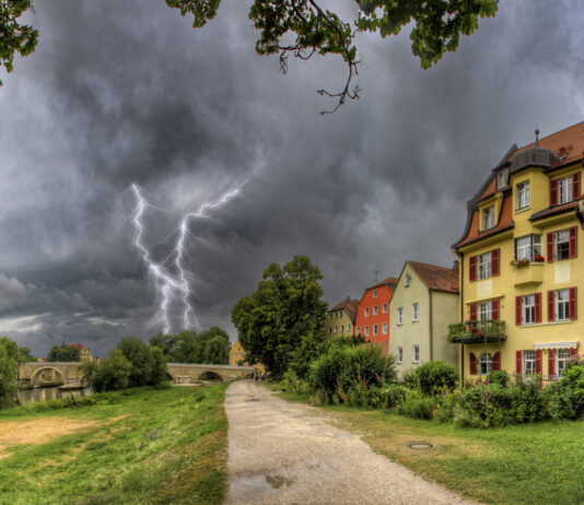 Ein Blitz ist im Hintergrund einer Stadt vor einem drohenden Gewitter zu sehen.