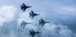 Sechs Kampfflugzeuge fliegen in Formation durch die Wolken. Es handelt sich um Bundeswehr-Jets, die Kommandos üben. Auf dem Bild sind nur die Silhouetten der Flieger, in denen die Soldaten sitzen, zu erkennen.