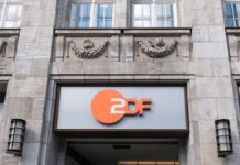 Der Eingang des ZDF-Gebäudes. Dieser befindet sich in einem sehr alten, historischen Gebäude. Auf einem grauen Hintergrund ist das orange-weiße Logo des ZDF angebracht.