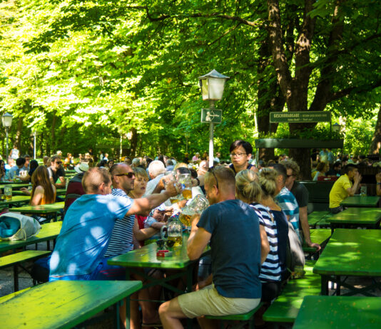 Viele Menschen auf Bierbänken mit Bier vor sich. Die Menschen stoßen gemeinsam an.