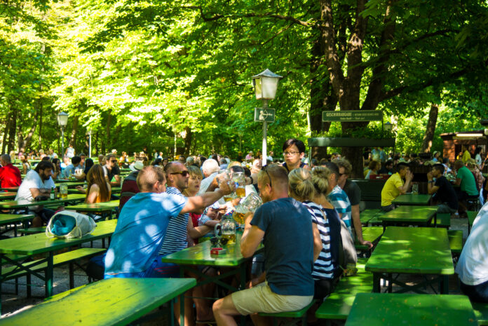 Viele Menschen auf Bierbänken mit Bier vor sich. Die Menschen stoßen gemeinsam an.