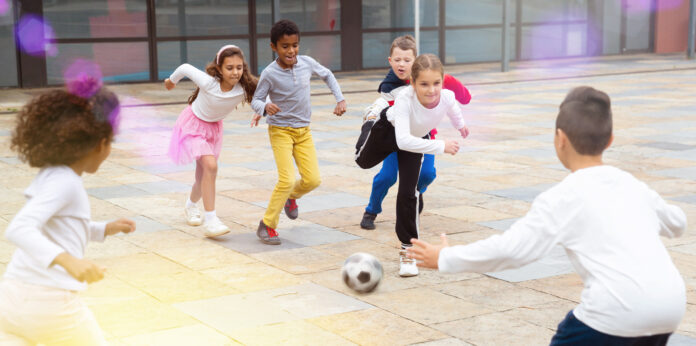 Jungen und Mädchen spielen gemeinsam auf dem Schulhof Fußball