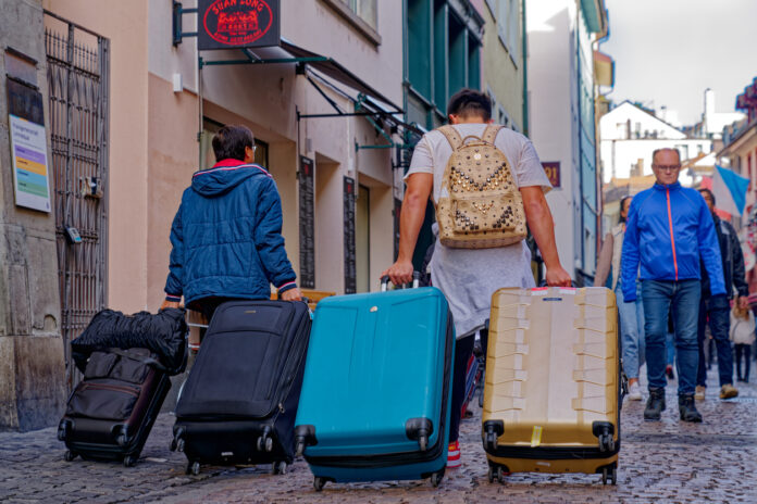Touristen spazieren durch die Altstadt einer Stadt und ziehen ihre Rollkoffer hinter sich her. Sie haben vorher die Koffer und Reisetaschen gepackt und sind jetzt zu Fuß durch die Innenstadt auf dem Weg zum Hotel oder zur Ferienwohnung.