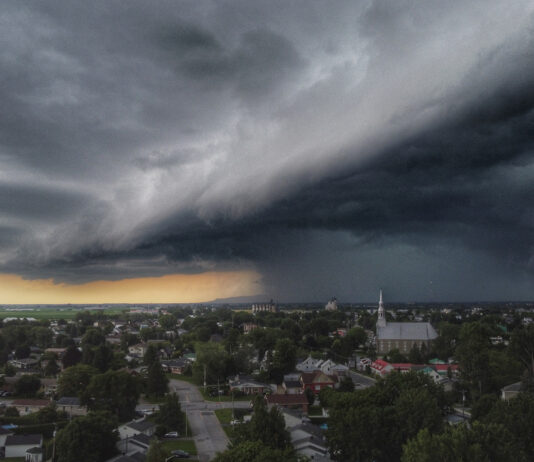 Ein gewaltiger Sturm zieht über eine Stadt her. Am Horizont ist noch ein Teil des guten Wetters zu sehen, während der Sturm einen großen Teil bereits mit seiner dichten Wolkendecke eingenommen hat.