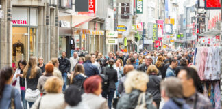 Viele Menschen in einer Einkaufsstraße mit mehreren Shops beim Bummeln. Es herrscht dichtes Gedränge und die Seiten füllen verschiedene Schilder großer und bekannter sowie kleiner Einzelhändler für Bekleidung, Deko und diverses andere.