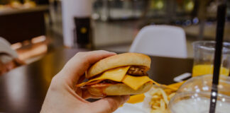 Eine Hand hält einen Burger mit Käse. Daneben stehen Milkshakes.