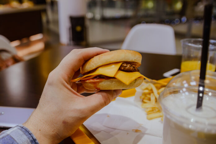 Eine Hand hält einen Burger mit Käse. Daneben stehen Milkshakes.