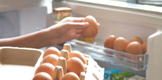 Eine Hand nimmt sich ein Ei aus dem Eierkarton, der im Kühlschrank gelagert ist.