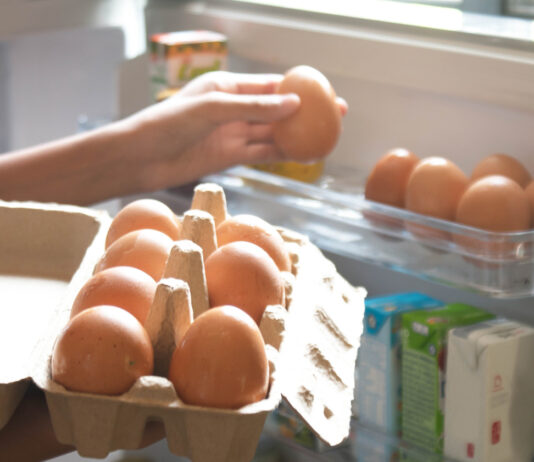 Eine Hand nimmt sich ein Ei aus dem Eierkarton, der im Kühlschrank gelagert ist.