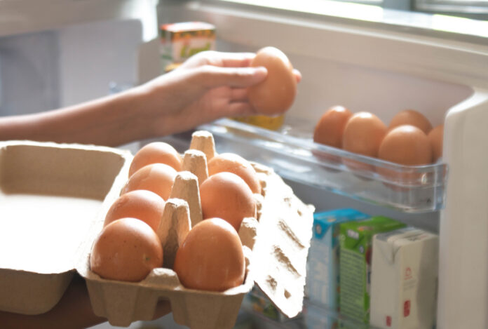 Eine Hand nimmt sich ein Ei aus dem Eierkarton, der im Kühlschrank gelagert ist.